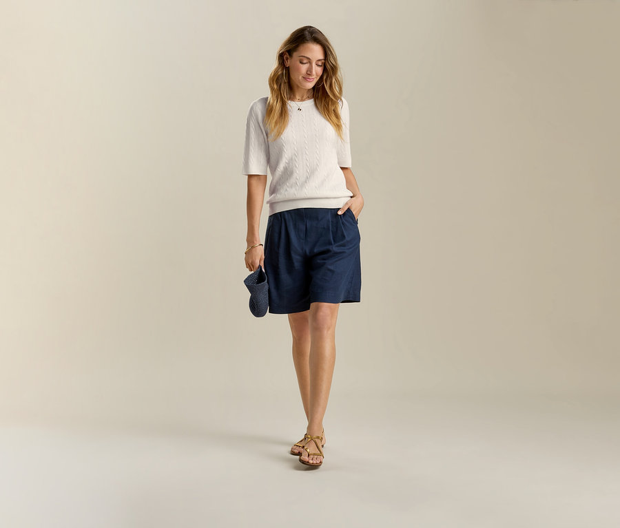 Žena v tmavomodrých ľanových bermudách a sandáloch. V ruke drží tmavomodrú čiapku.