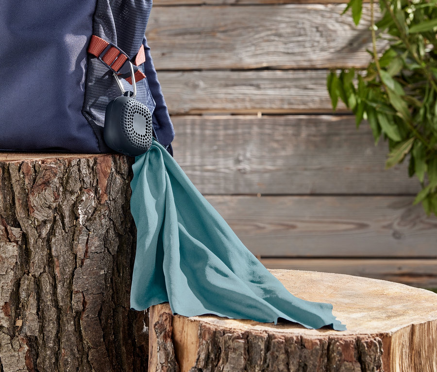 Tmavo modrý batoh leží na pni stromu, ku ktorému je pripevnený sivý reproduktor s tyrkysovou handričkou.