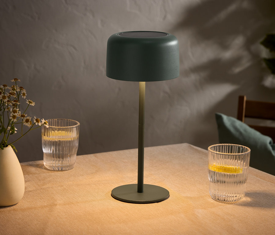 Stôl s vázou kvetov, dvoma pohármi s citrónmi a zelenou lampou.