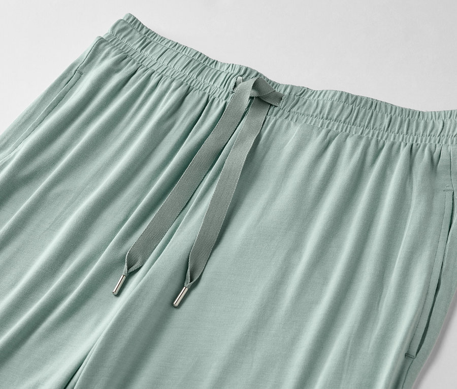 Detailný záber svetlozelených nohavíc so sťahovacou šnúrkou a vreckami.