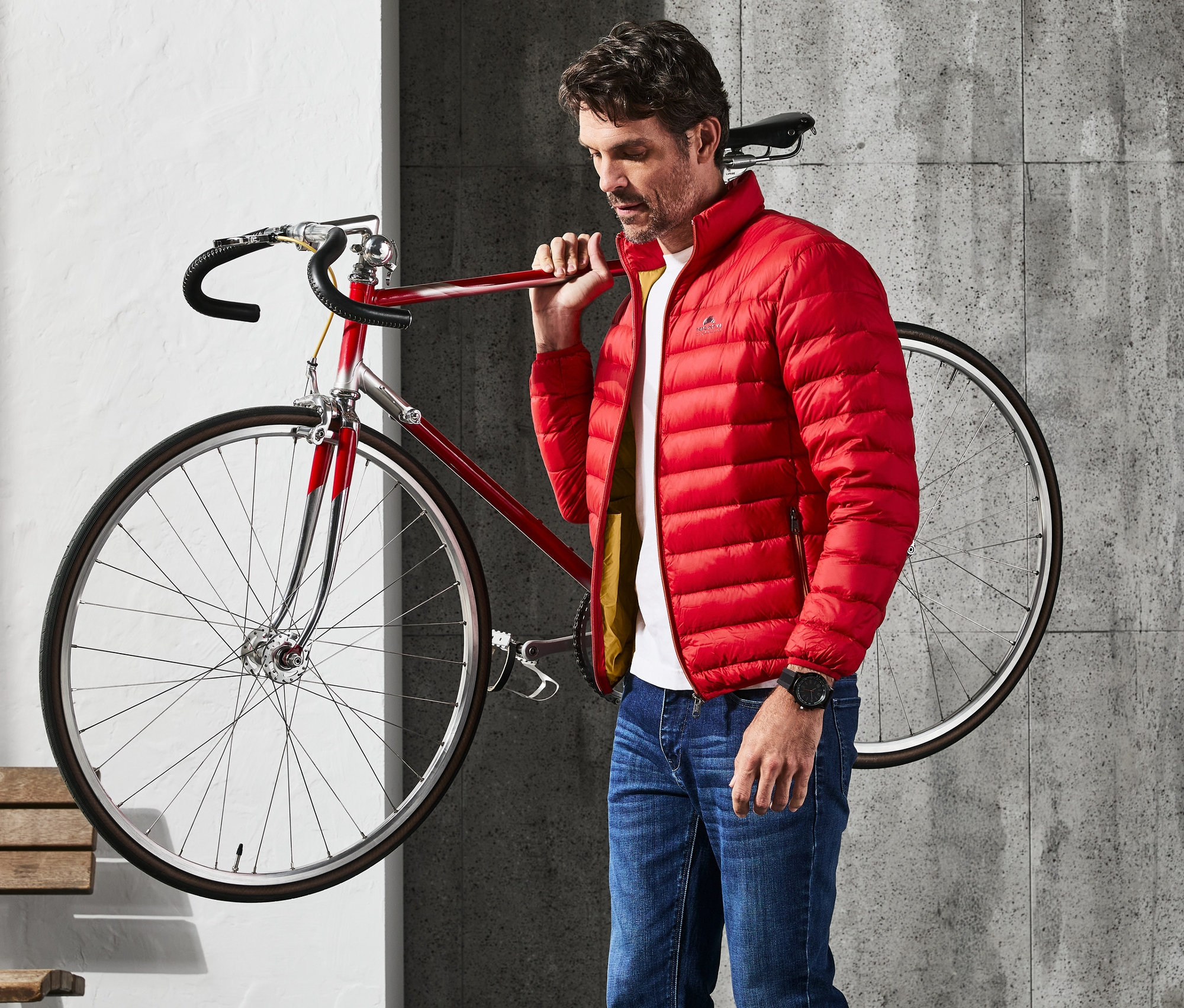 Muž nesie červenú páperovú bundu cez rameno vedľa červeného bicykla.