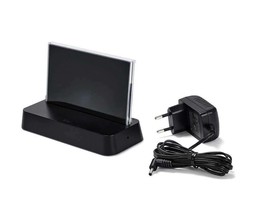 Čierna meteorologická stanica riadená rádiovým signálom s farebným LCD displejom a napájací adaptér na bielom pozadí.