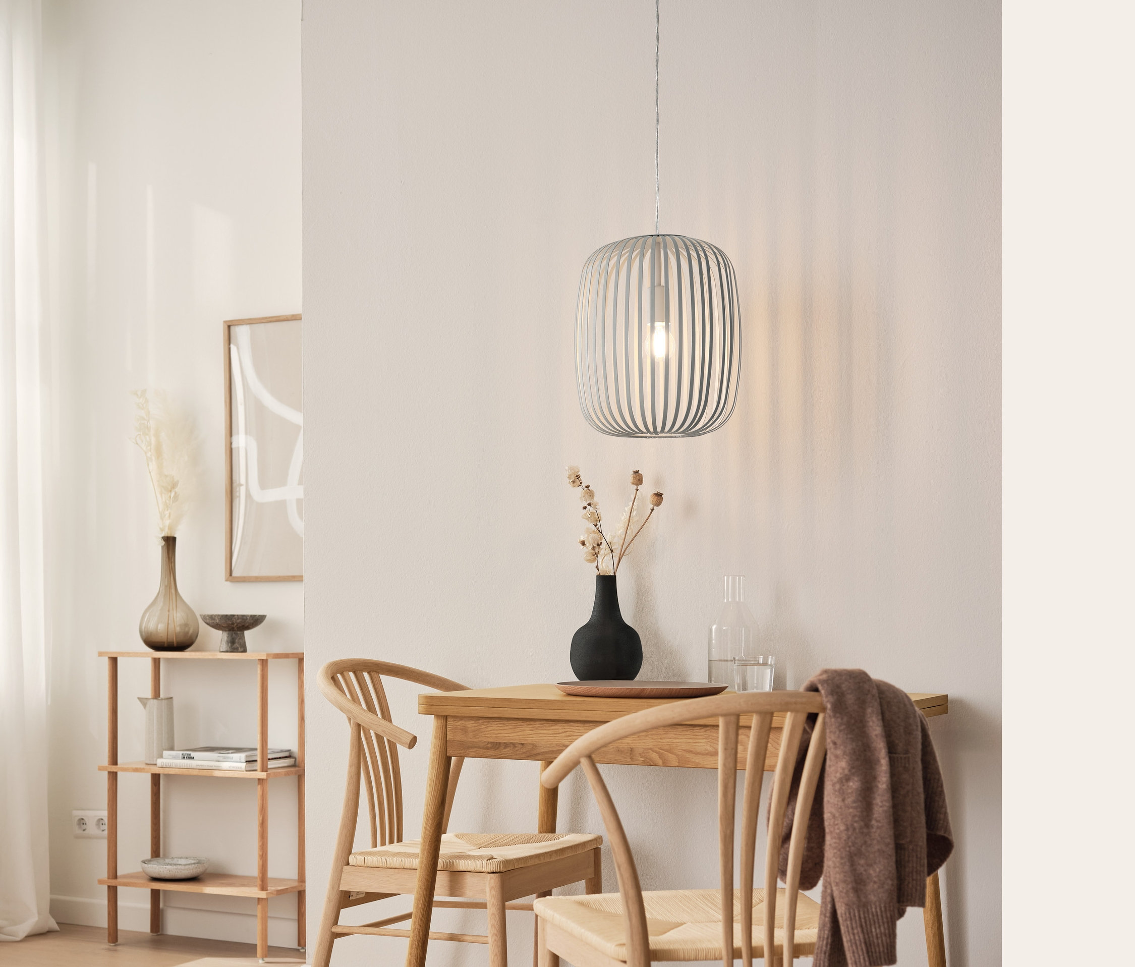 Jedálenský kút s rozkladacím jedálenským stolom, závesnou kovovou lampou a stojacím regálom.