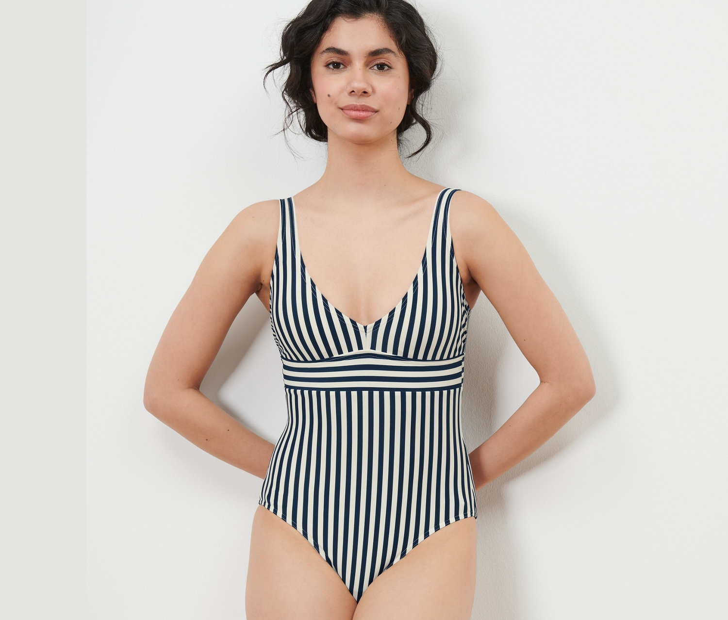 Žena pózuje v plavkách s modrými a bielymi pruhmi.