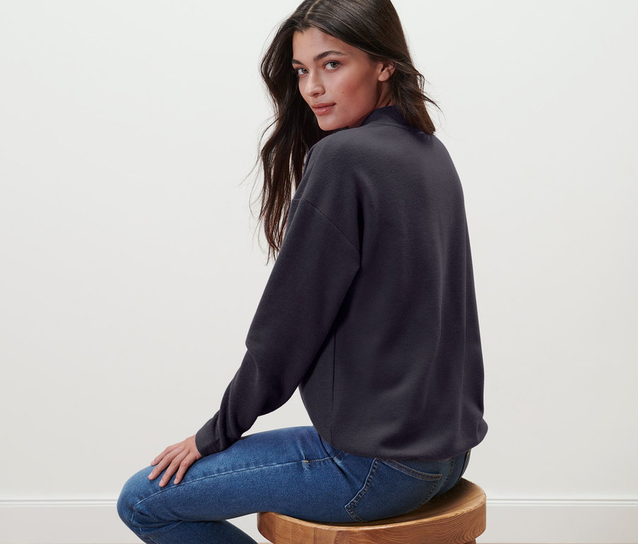 Žena sedí na stoličke a má na sebe mikinu so stojačikom.