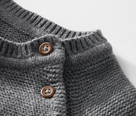 Detail detského pleteného pulóvra s hnedými gombíkmi.