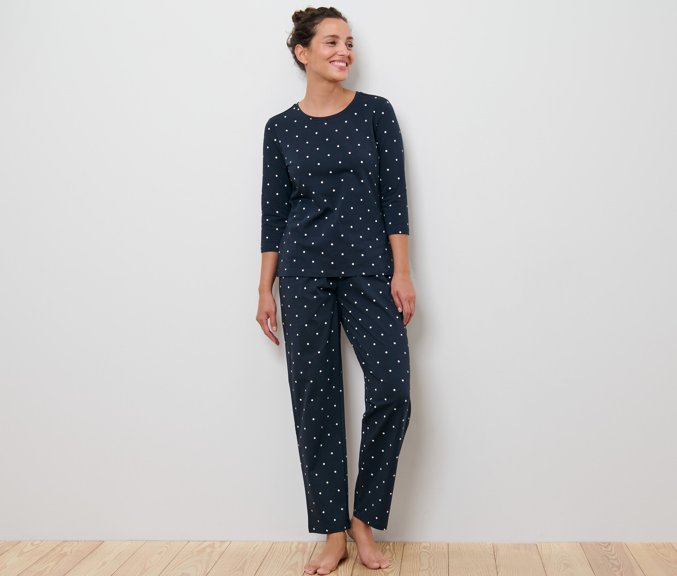 Žena stojí a má na sebe tmavomodré pyžamo s bodkami.