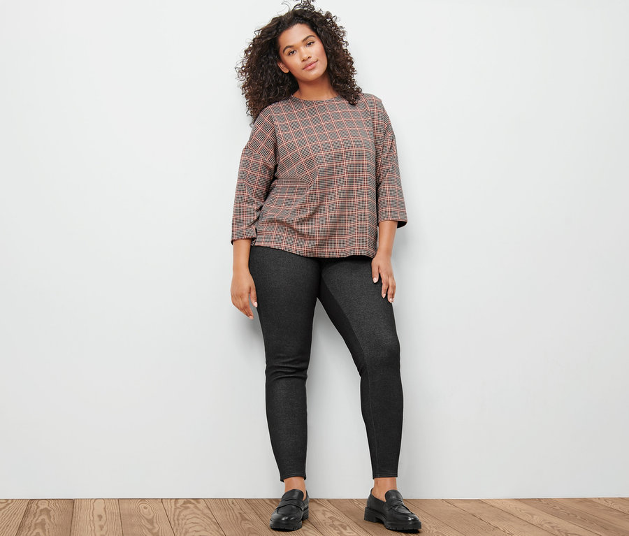 Žena pózuje v mikinovom tričku s trojštvrťovými rukávmi, kohútia stopa a v podšitých legínsach s džínsovým vzhľadom.