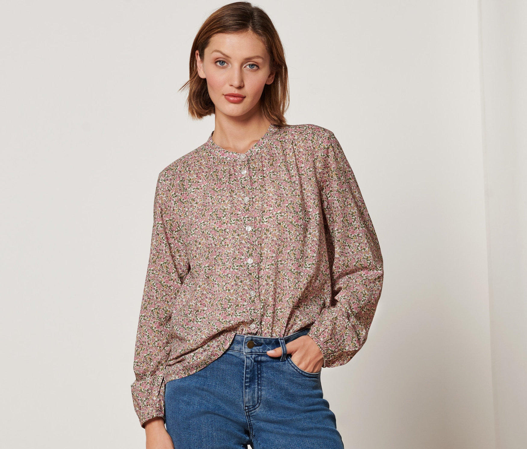 Žena má na sebe blúzku s kvetinovou potlačou a džínsy.