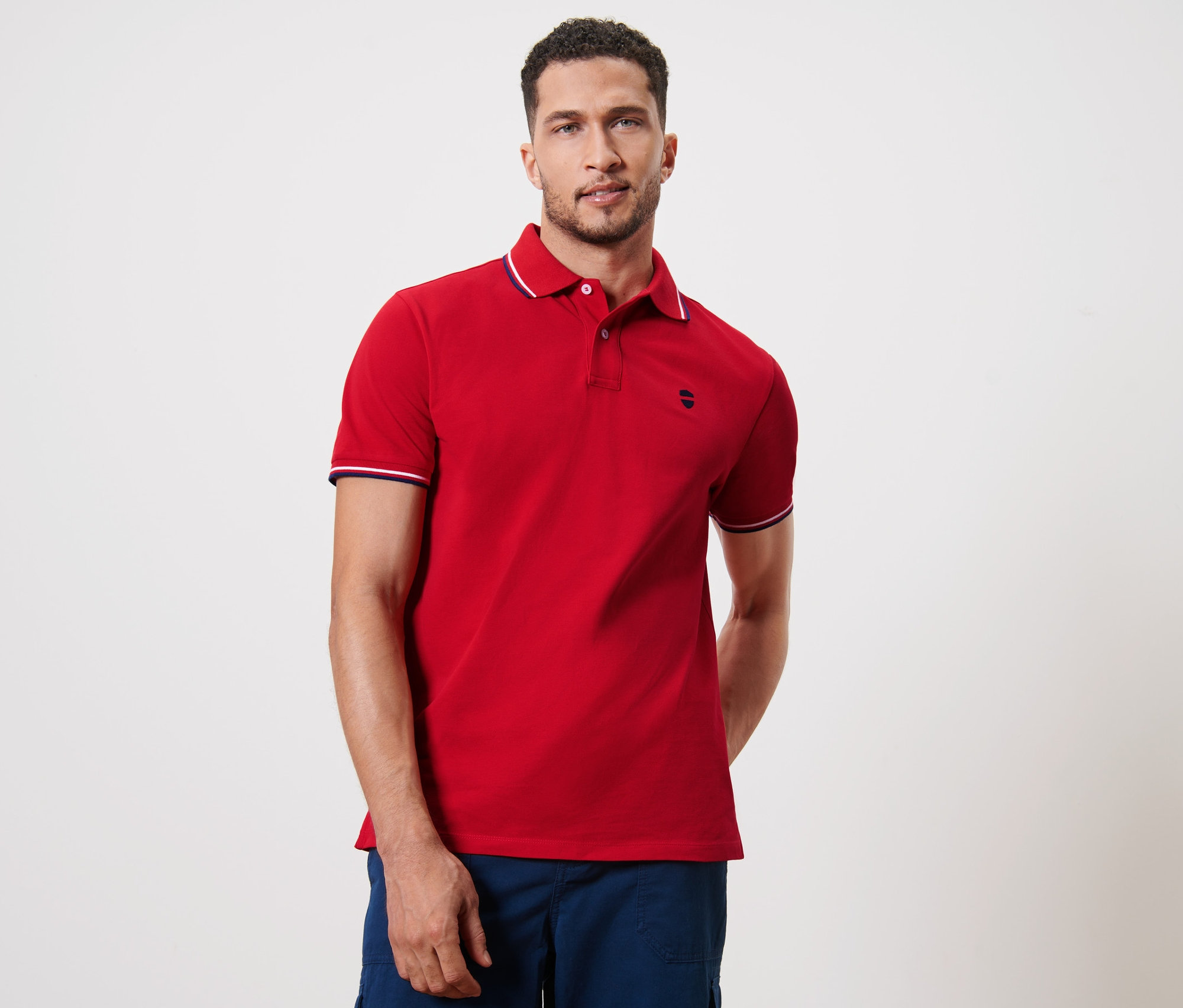 Muž pózuje v červenej piké polokošeli.