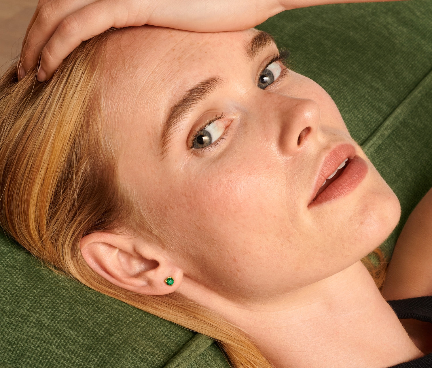 Blondína leží na zelenej pohovke a má na sebe napichovacie náušnice, súpravu.