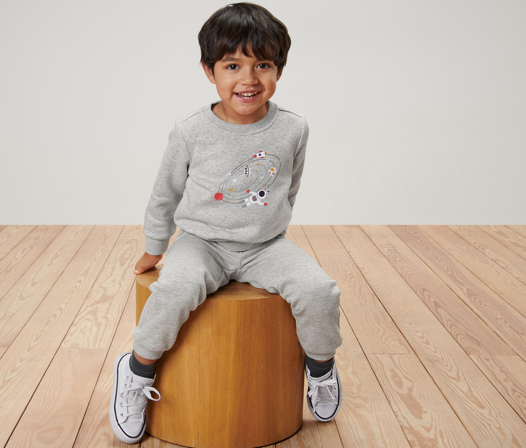 Chlapec sedí na stoličke a má na sebe detskú mikinu, vesmír.