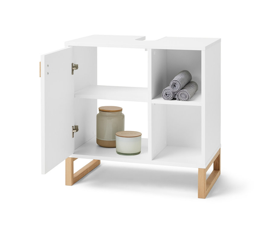 Otvorená biela umývadlová skrinka s dvierkami a poličkou naboku. V bočnej časti sú zrolované sivé uteráky a vo vnútri skrinky sú sviečky a dóza.