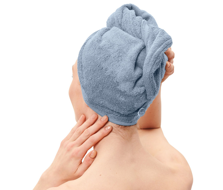 Žena s uterákovým turbanom svetlomodrej farby na hlave a uterákom rovnakej farby ovinutým okolo tela.