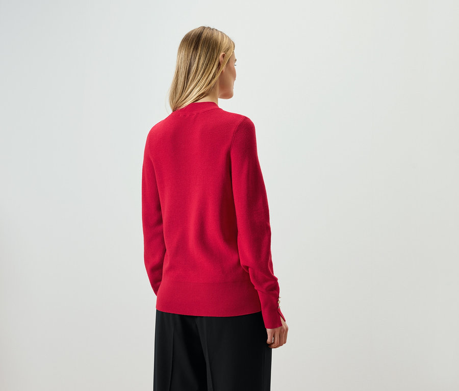 Zozadu je vidieť žena s blond vlasmi v červenom svetri a čiernych nohaviciach.