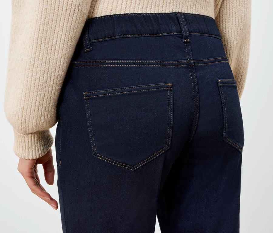 Pohľad zozadu na ženu v tmavomodrých džeginách a béžovom svetri.