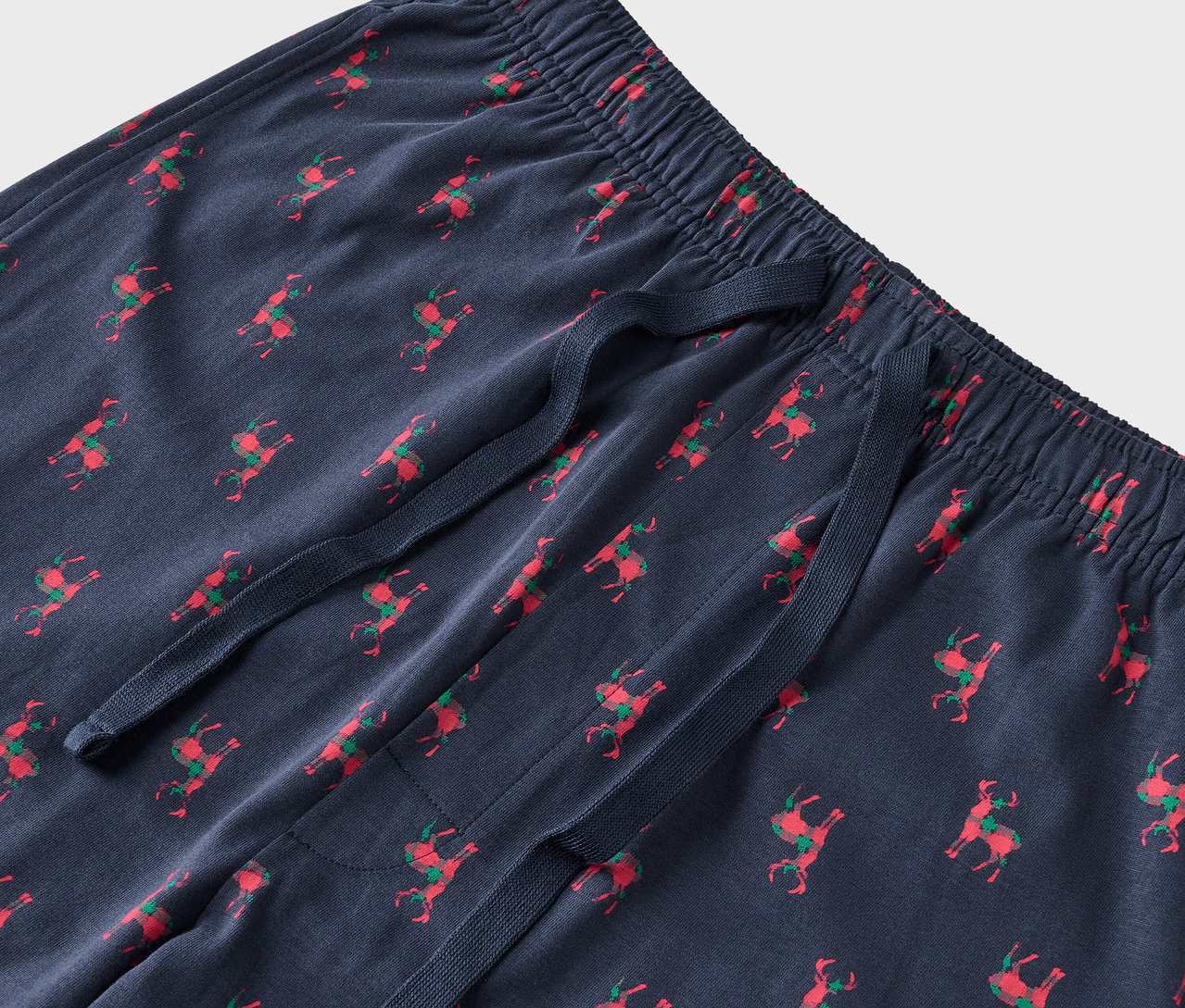 Detail modrých pyžamových nohavíc s červenými sobmi a zelenými sedlami.