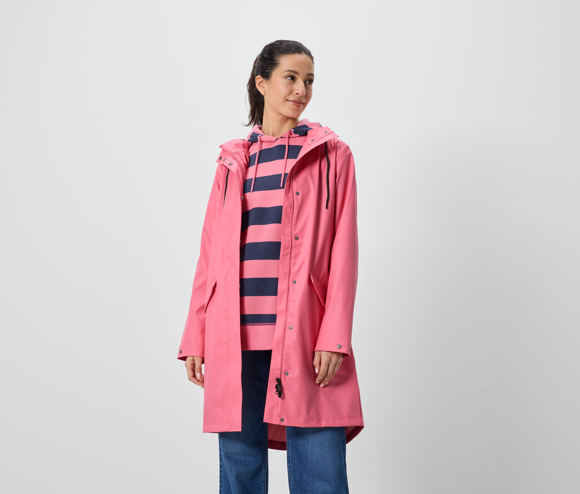 Žena má na sebe ružový kabát a pruhovanú mikinu s kapucňou.