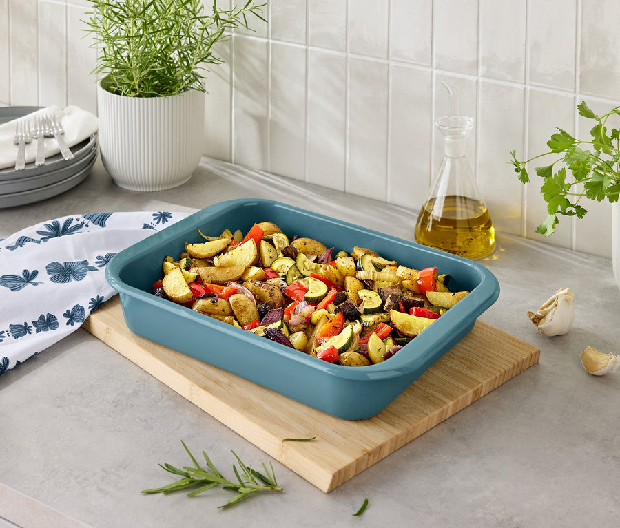 Pečené zemiaky so zeleninou v modrej zapekacej mise na drevenej doske.