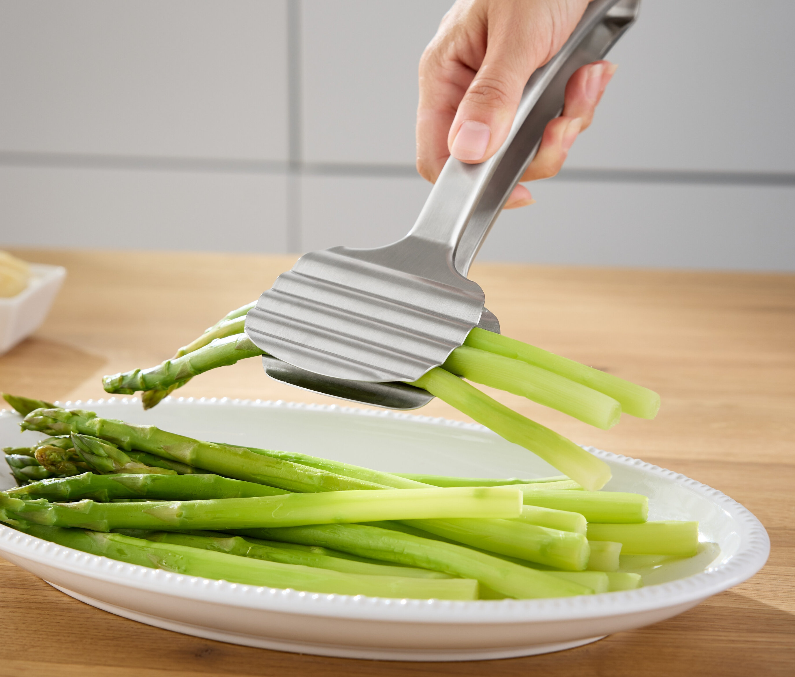 Ruka drží strieborné kliešte na špargľu nad miskou so zeleným špargľou.