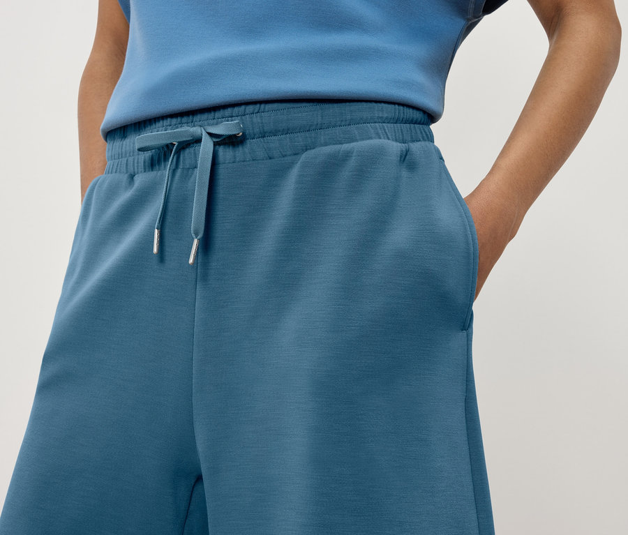 Detail dámskych modrých teplákových nohavíc s rukou vo vrecku.