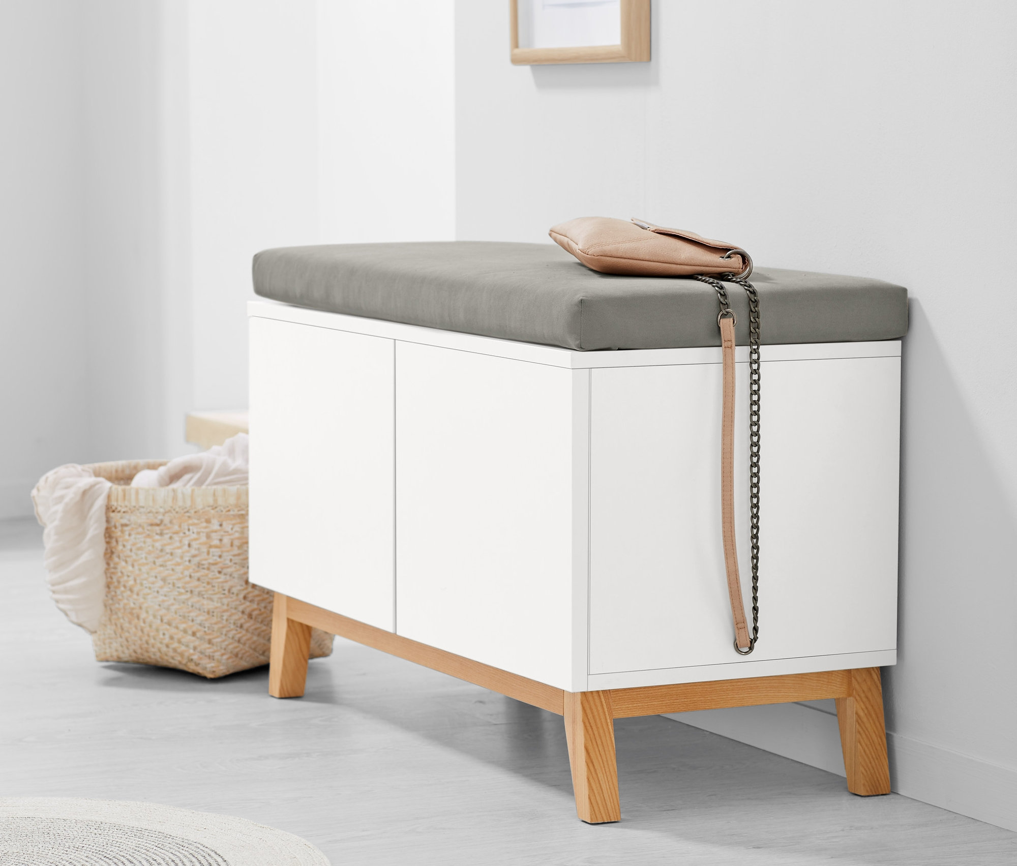 Biela lavica s úložnými priehradkami a sivou poduškou. Na lavici leží béžová kabelka.