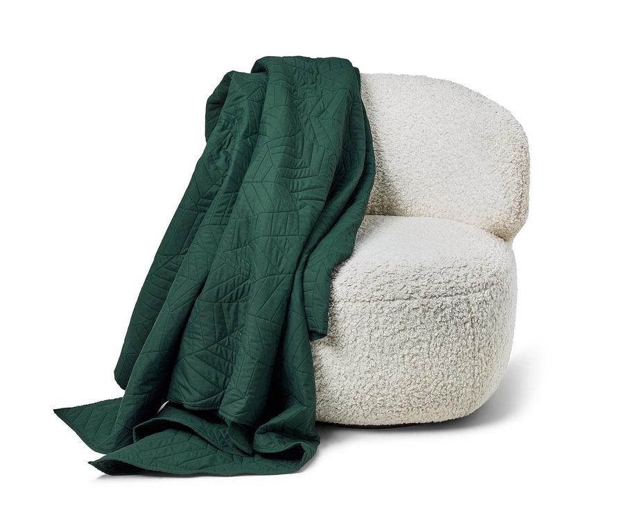 Tmavozelená prešívaná prikrývka na posteľ (230 x 250 cm) leží na bielom kresle.