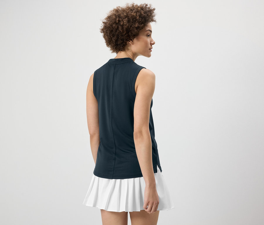 Žena chrbtom k fotoaparátu má na sebe tmavomodrý funkčný top a bielu sukňu.