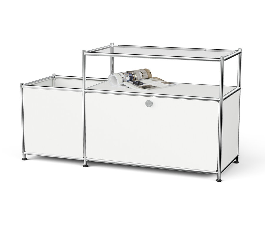 Biely modulárny úložný systém s chrómovaným rámom a sklenenými policami, na hornej polici je zrolovaný časopis.