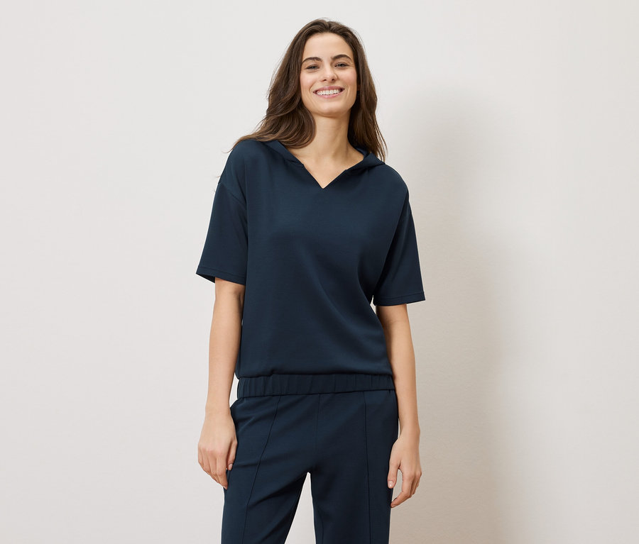 Usmievavá brunetka má na sebe tmavomodrý komplet: blúzku s krátkym rukávom a nohavice.