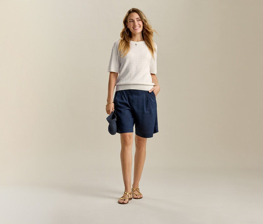 Žena v svetlom tope a tmavomodrých ľanových bermudách Leinen-Bermuda-Shorts s rukou vo vrecku.