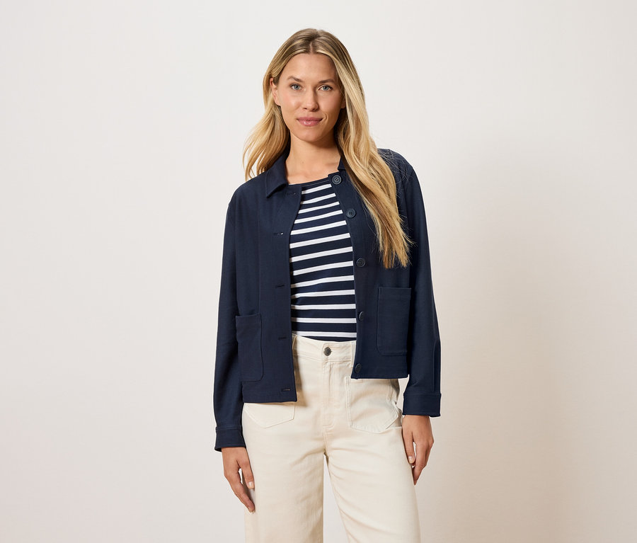 Žena má na sebe tmavomodrú bundu cez pruhovaný top a krémové nohavice.