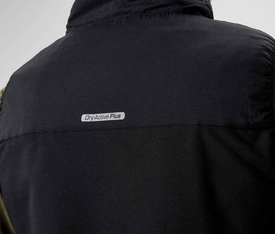 Detailný záber na zadnú časť čiernej vesty s nápisom "Dry Active Plus" oblečenej na olivovozelenej košeli s dlhým rukávom.