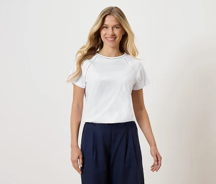 Žena má na sebe biele tričko a tmavomodré culottes na bielom pozadí.