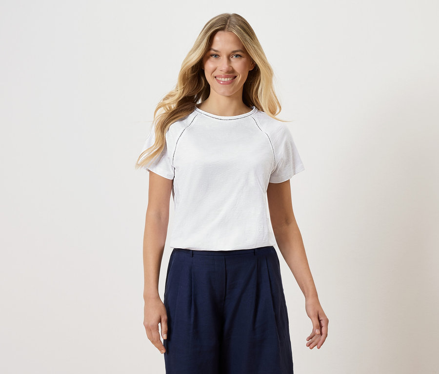 Žena má na sebe biele tričko a tmavomodré culottes na bielom pozadí.