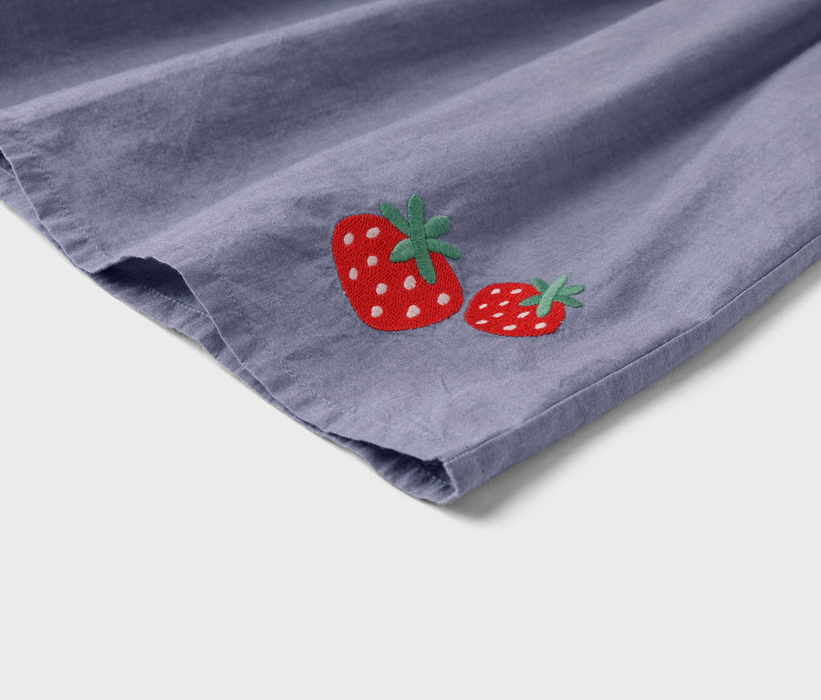 Detailný pohľad na fialovú látku s dvoma vyšitými jahodami.
