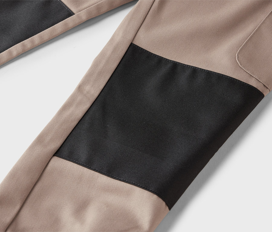 Detail béžových nohavíc s čiernymi záplatami.