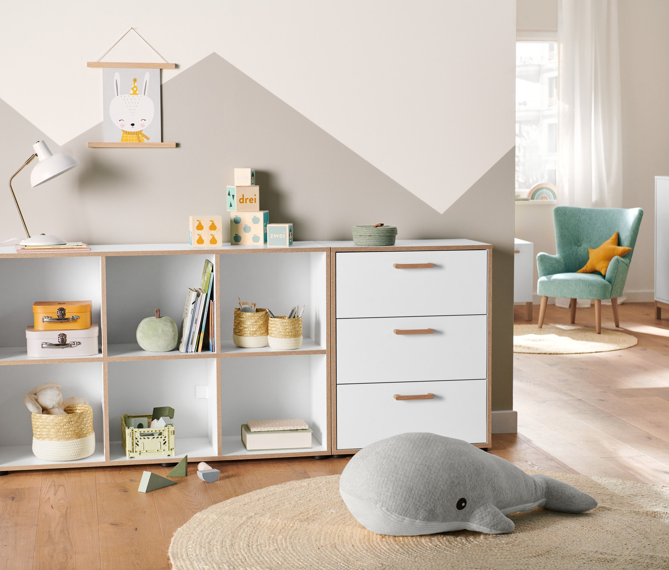 Izba s komodou s dyhovanou hranou, úložnými košíkmi a veľkou plyšovou veľrybou na okrúhlom koberci.