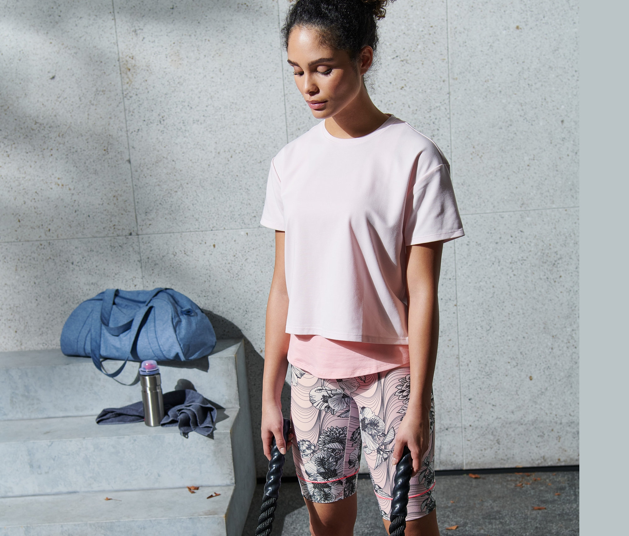 Žena cvičí s lanami v ružových funkčných cyklistických nohaviciach.