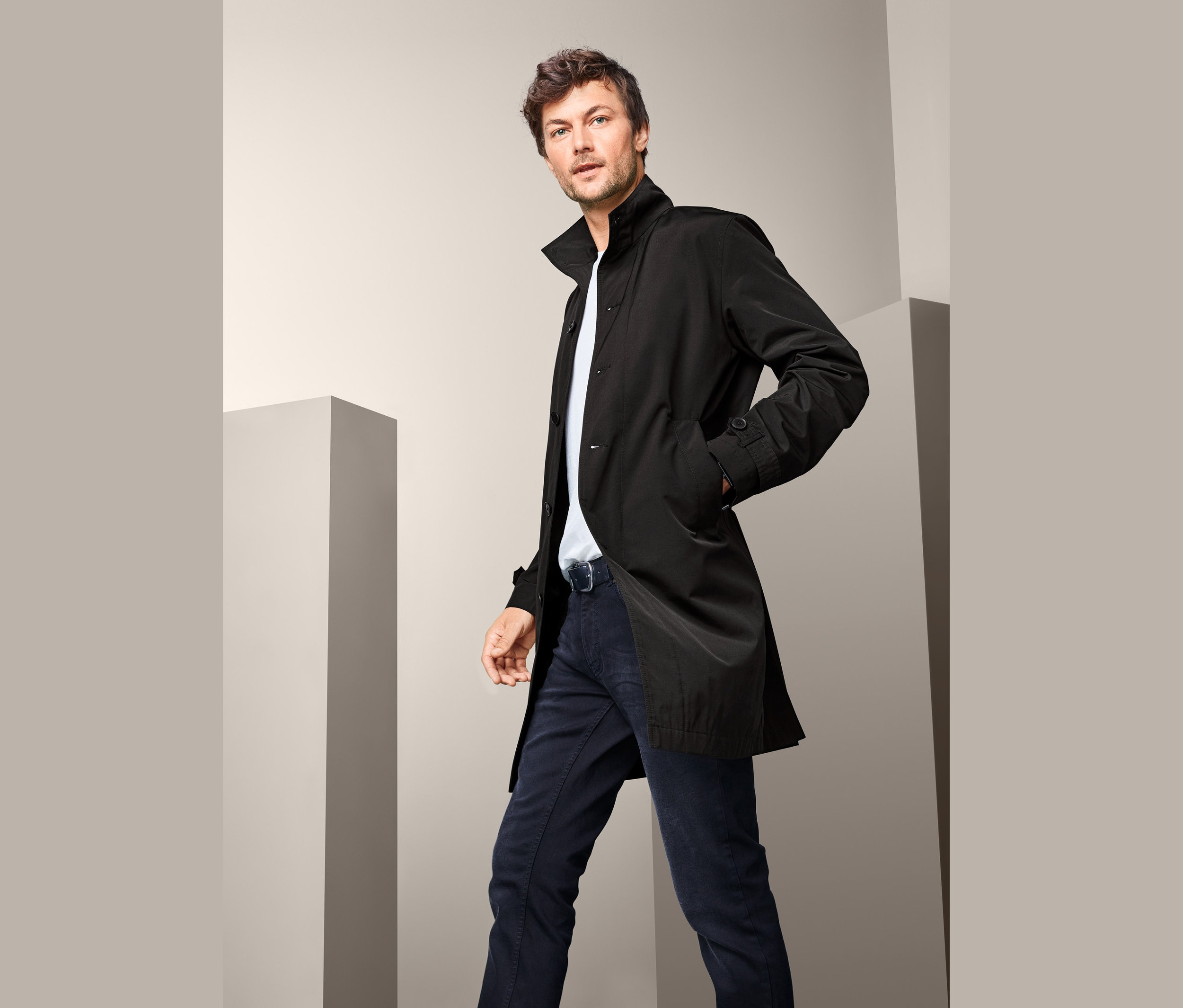 Muž pózuje v čiernom kabáte so stojačikom.