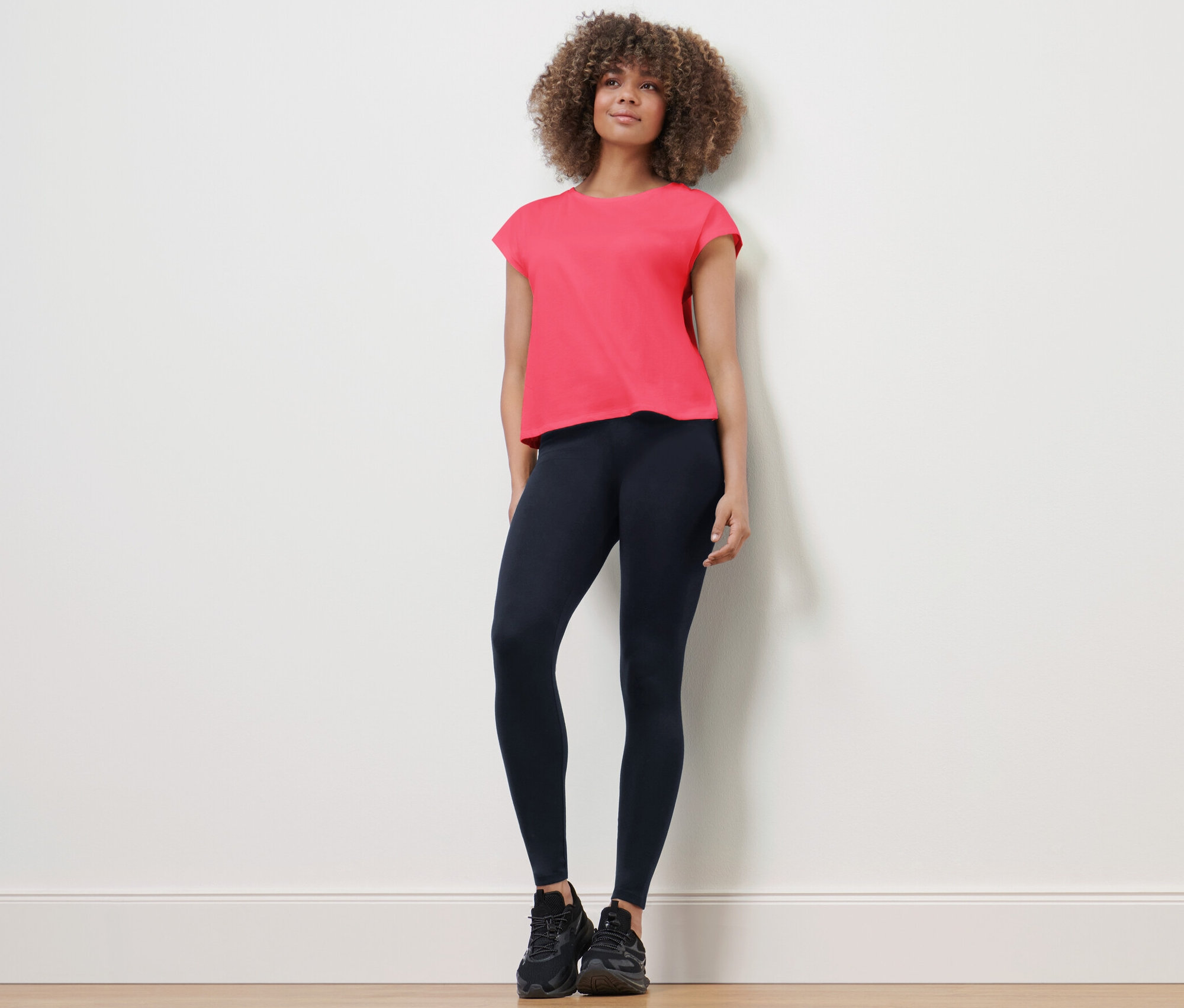 Žena stojí a má na sebe športové legíny a tričko.