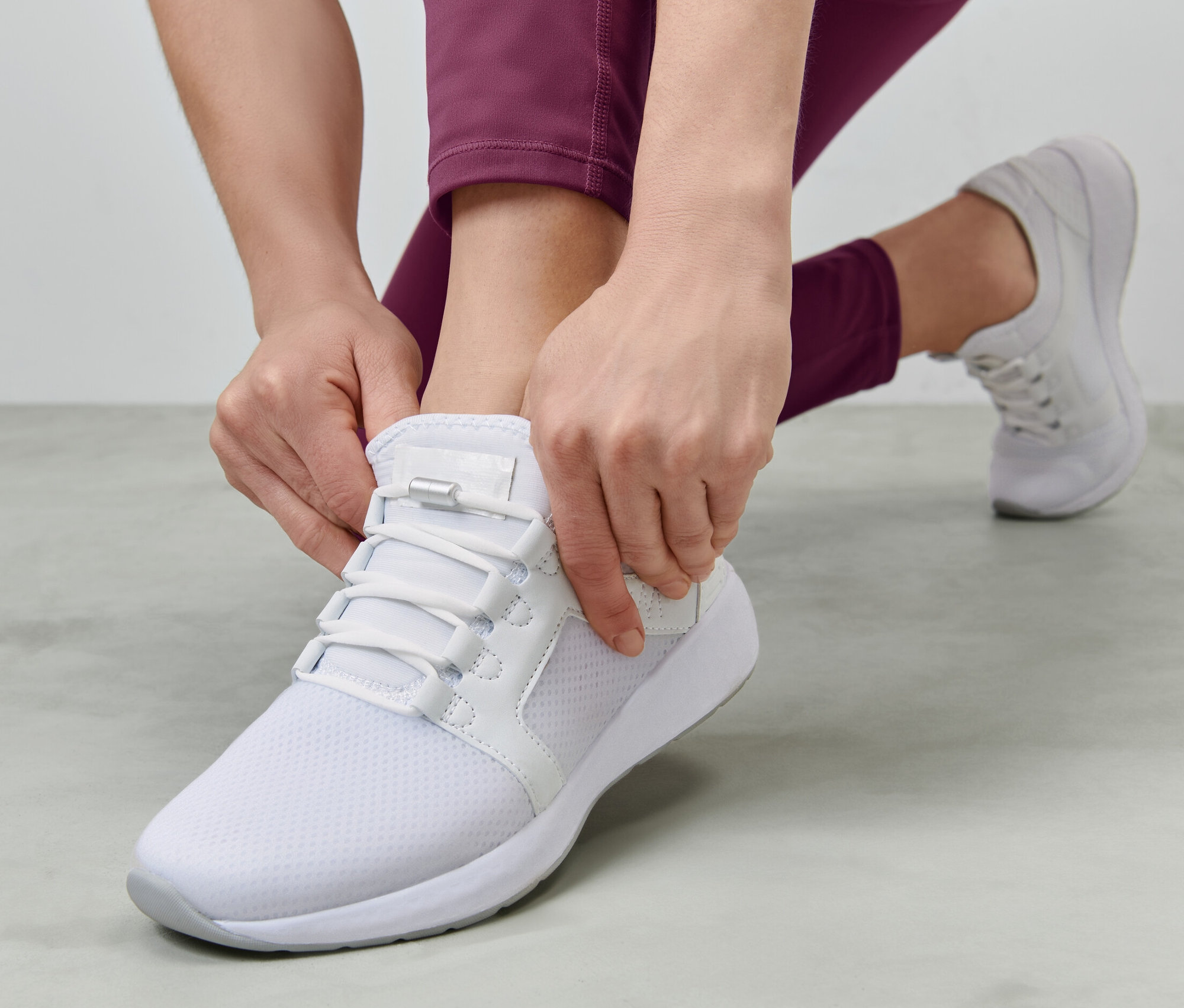 Žena si zaväzuje elastické šnúrky na bielej topánke.
