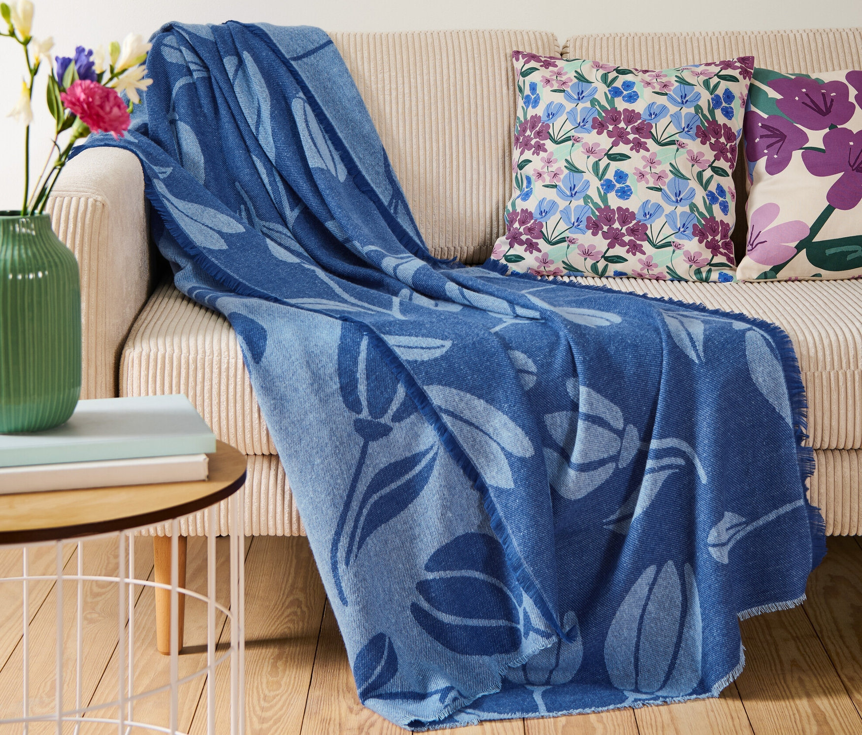 Na béžovej pohovke leží modrá deka so strapcami.