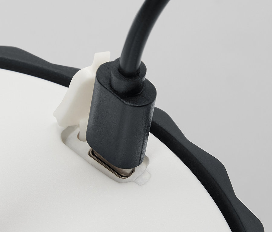Detail Malej stolnej lampy LED s čiernym napájacím káblom zapojeným do bielej základne.