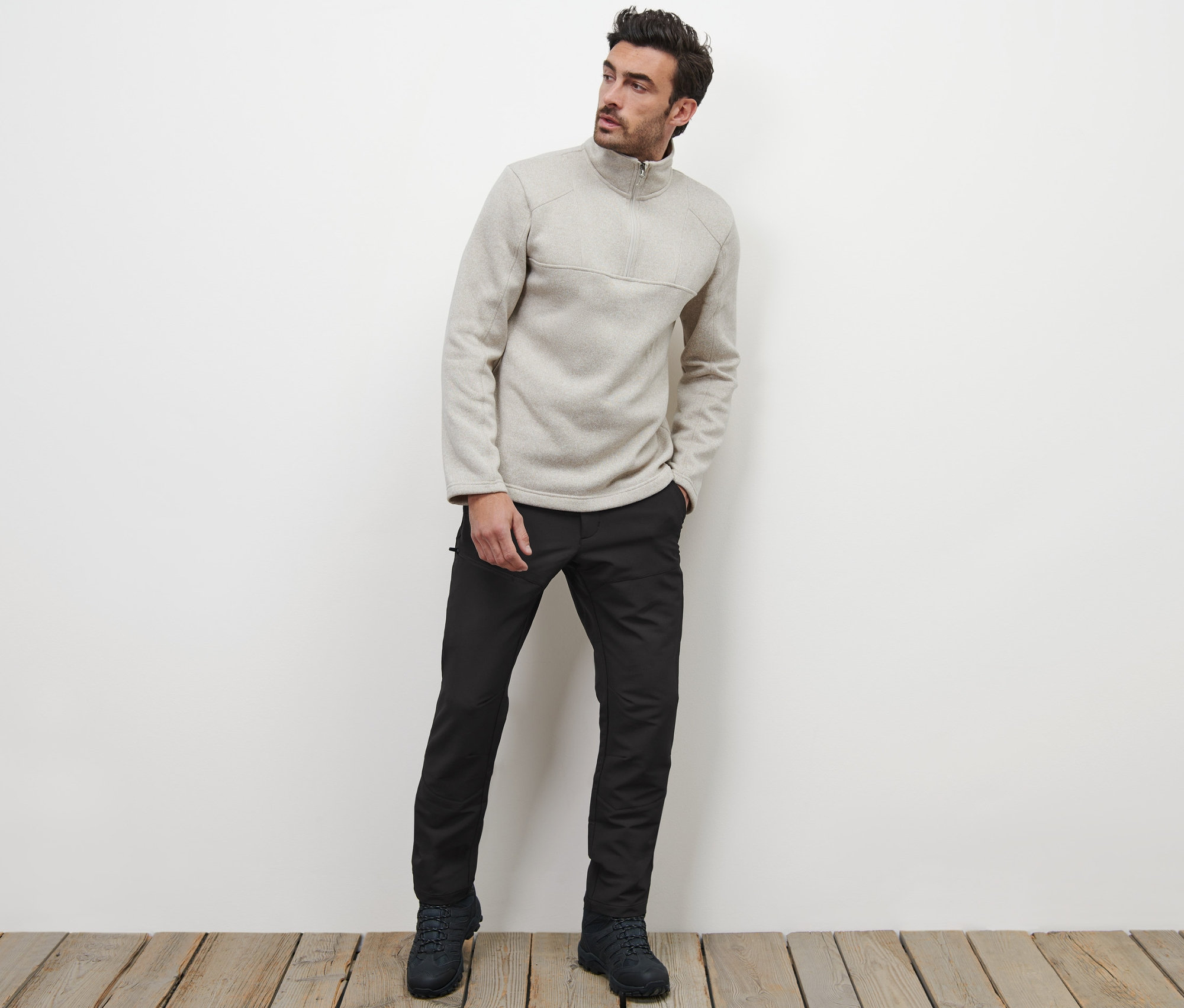 Muž pózuje na drevenej podlahe a má na sebe termonohavice a mikinu so zipsom.