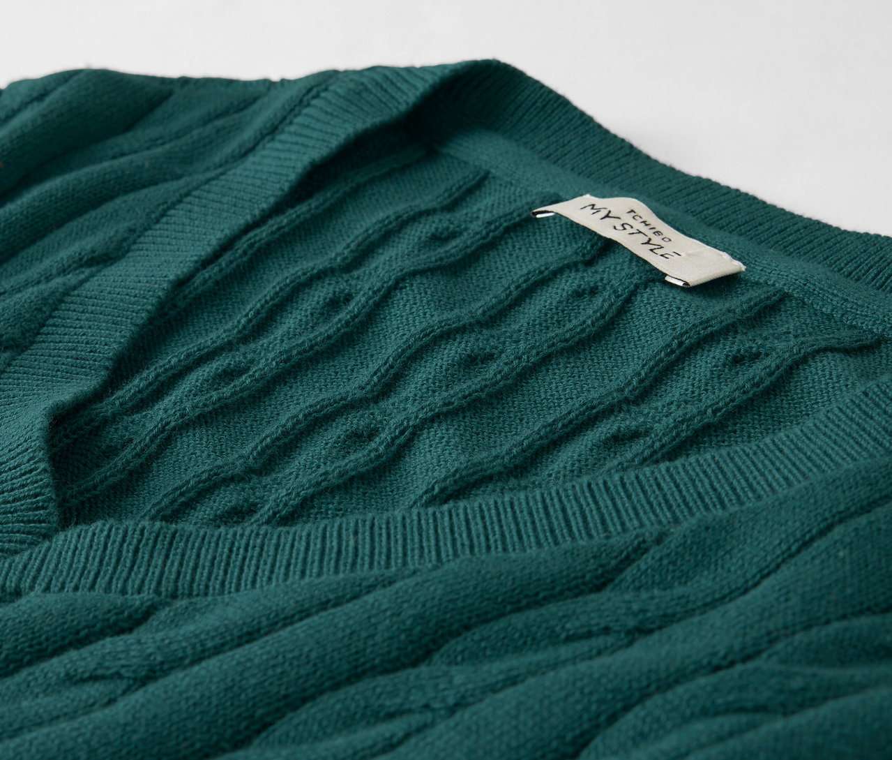 Detailný záber na smaragdovo zelený pletený sveter s vrkočovým vzorom a visačkou.