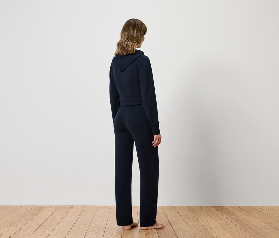 Žena chrbtom k fotoaparátu má na sebe tmavomodrú mikinu s kapucňou a tepláky.