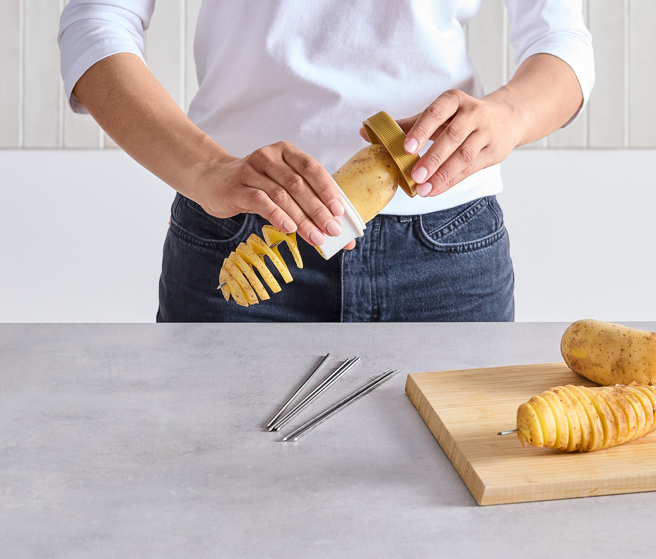 Osoba krája zemiak na špirálu pomocou špeciálneho krájača. Na stole leží nakrájaný zemiak na špajli a surový zemiak.