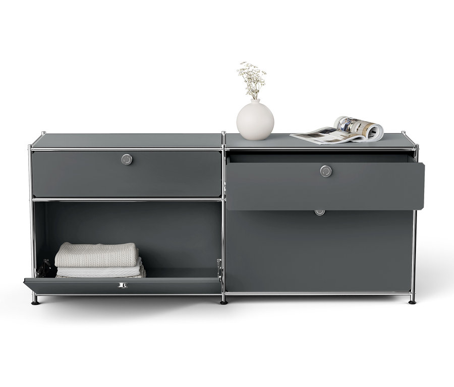 Sivá skrinka so strieborným rámom, otvorená zásuvka, biela váza s kvetmi a časopis navrchu.