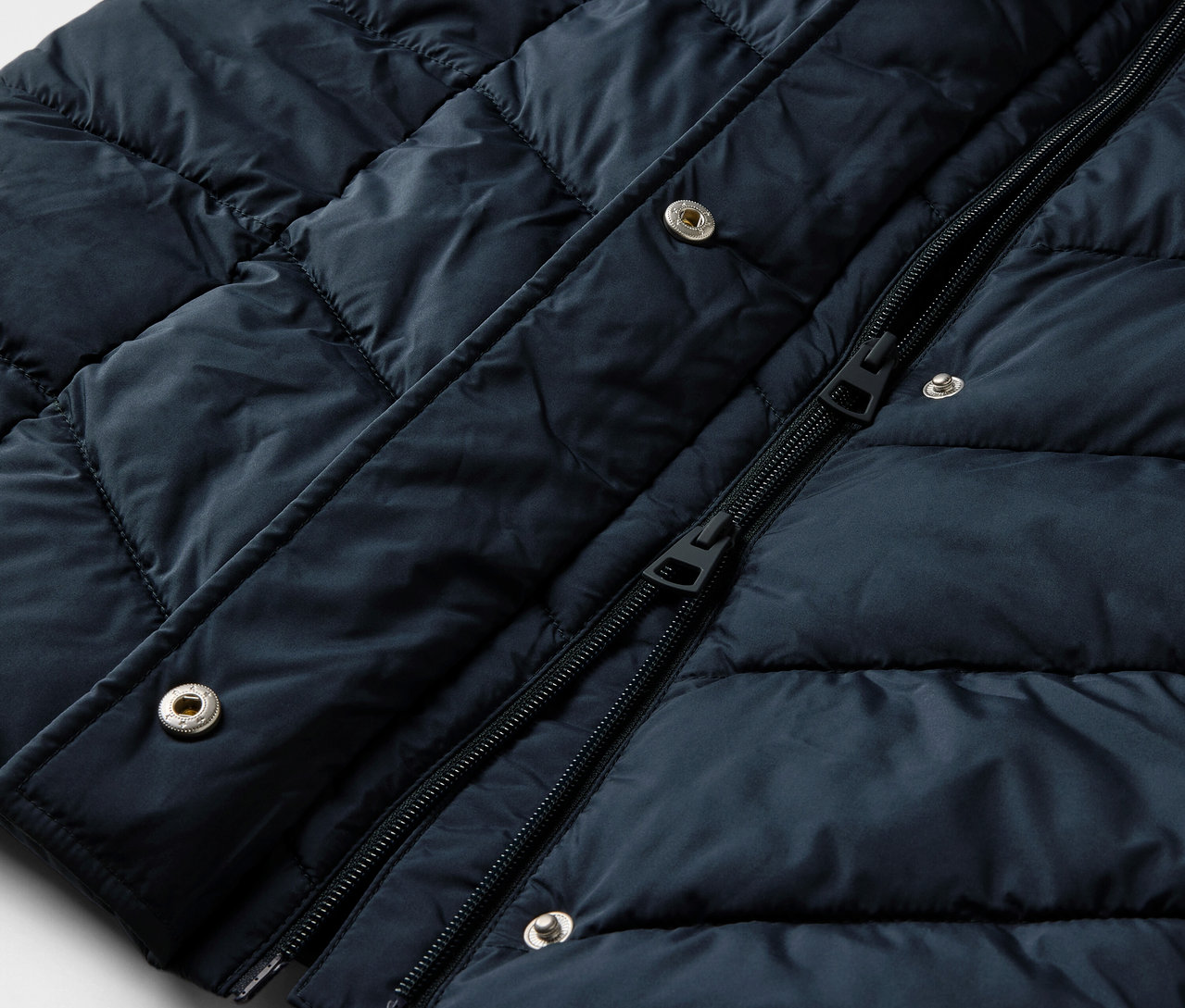 Detailný záber na tmavomodrý prešívaný kabát s kapucňou.